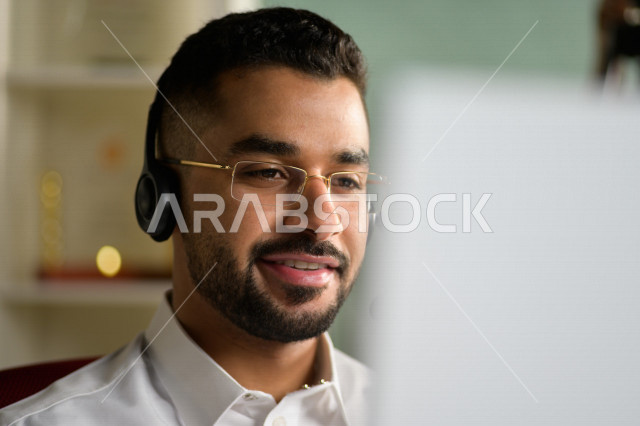 A Saudi Arabian Gulf employee working in customer service and wearing a headset, inquiries and inquiries, answering customer questions, making video calls through a computer, eyeglasses, follow-up and work development