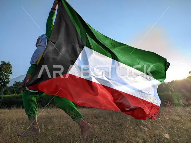 أعياد ومناسبات وطنية، الاحتفال بالعيد الوطني الكويتي 25 فبراير, حب الوطن والانتماء إليه, إظهار مشاعر الفخر بالهوية الكويتية، صورة لفتاة عربية خليجية إماراتية محجبة تركض رافعة علم دولة الكويت باعتزاز عاليا