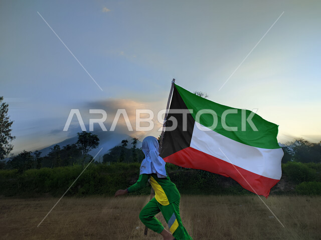 أعياد ومناسبات وطنية، الاحتفال بالعيد الوطني الكويتي 25 فبراير, حب الوطن والانتماء إليه, إظهار مشاعر الفخر بالهوية الكويتية، صورة لفتاة عربية خليجية إماراتية محجبة تركض رافعة علم دولة الكويت باعتزاز عاليا