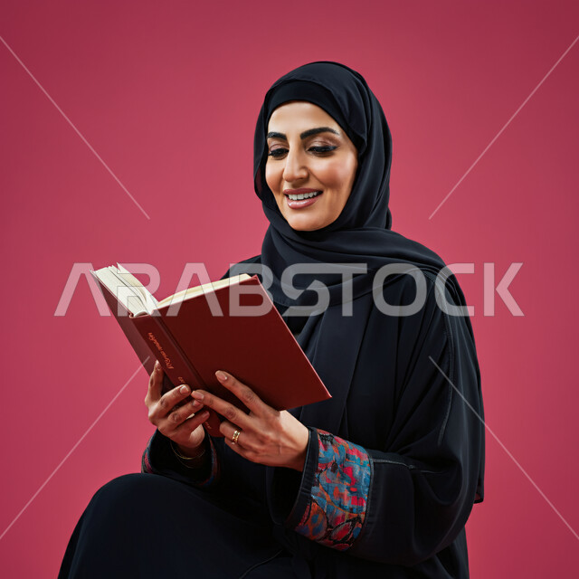 الاستمتاع بقراءة الكتب والقصص والروايات، إنجاز الواجبات اليومية، قضاء الوقت بالقراءة والتعلم والتثقف، بورتريه مقرب لامرأة عربية سعودية خليجية ترتدي الحجاب والعباءة تحمل بيديها كتاب، ثقافة التعلم الذاتي، خلفية حمراء