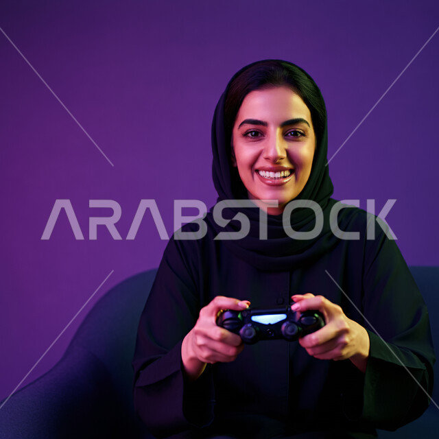 الاستمتاع في قضاء أوقات الفراغ بلعب الفيديو غيمز، إيماءات وتعابير وجه ويدين تدل على الفوز والانتصار، بورتريه مقرب لإمرأة عربية سعودية خليجية ترتدي الحجاب والعباءة تجلس على كرسي مريح وتحمل بيدها عصا التحكم وتلعب بألعاب الفيديو، خلفية بنفسجية