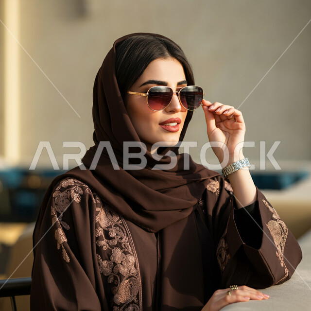 جمال النساء السعوديات، الاهتمام بالمظهر الخارجي، مفهوم الأنوثة والأناقة والشياكة، أزياء محجبات عصرية حديثة، صورة مقربة لامرأة عربية خليجية سعودية ترتدي الحجاب والعباءة تضع النظارات الشمسية تنظر إلى شيء ما بإيماءات الثقه بالنفس