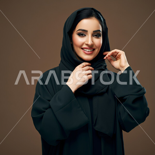 Chic, elegance and care for the external appearance, the concept of softness and femininity, a close-up portrait of a Saudi Arabian Gulf woman wearing a black abaya looking at the camera with expressions of joy, happiness and pleasure, the beauty of Saudi women, brown background