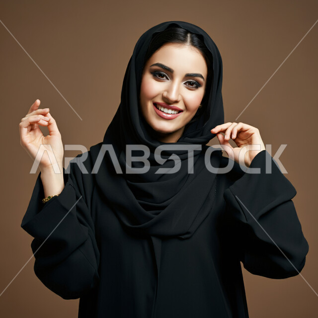 الشياكة والأناقة والاعتناء بالمظهر الخارجي، مفهوم النعومة والأنوثة، بورتريه مقرب لأمراة عربية خليجية سعودية ترتدي العباءة السوداء تنظر الى الكاميرا بتعابير الفرح والسعادة والسرور، جمال النساء السعوديات، خلفية بني