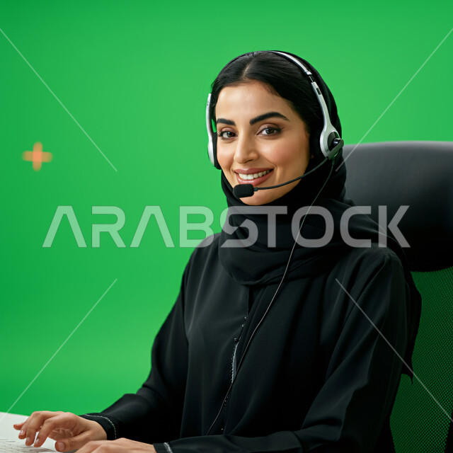 استخدام التقنيات الحديثة، بورتريه مقرب لسيدة عربية سعودية خليجية ترتدي الحجاب والعباءة تعمل في الدعم الفني وخدمة العملاء، ارتداء سماعة الاتصال للإجابة عن الاستعلامات والاستفسارات، زيادة مستوى رضا العميل، خلفية خضراء، كروما