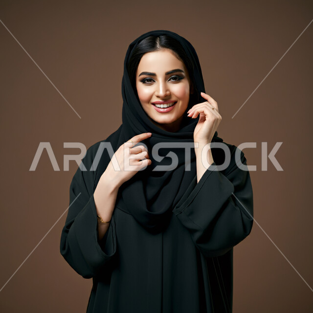 مفهوم النعومة والأنوثة، الشياكة والأناقة والاعتناء بالمظهر الخارجي، بورتريه مقرب لأمراة عربية خليجية سعودية محجبة مبتسمة ترتدي العباءة السوداء تنظر الى الكاميرا بتعابير الفرح والسعادة والسرور، خلفية بني