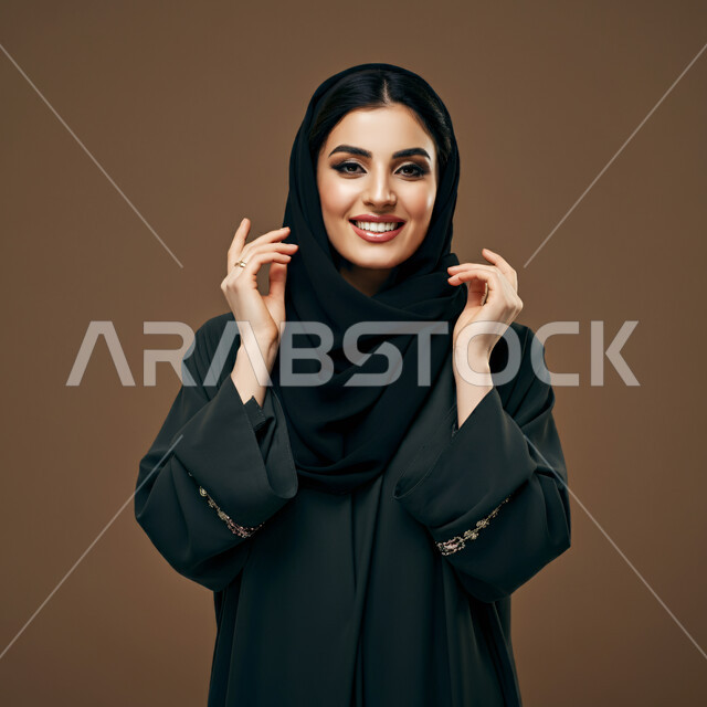 مفهوم النعومة والأنوثة، الشياكة والأناقة والاعتناء بالمظهر الخارجي، بورتريه مقرب لأمراة عربية خليجية سعودية محجبة مبتسمة ترتدي العباءة السوداء تنظر الى الكاميرا بتعابير الفرح والسعادة والسرور، خلفية بني