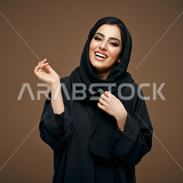 The concept of softness and femininity, chicness and elegance and taking care of one's appearance, a close-up portrait of a smiling veiled Saudi Arabian Gulf woman wearing a black abaya looking at the camera with expressions of joy, happiness and pleasure, brown background