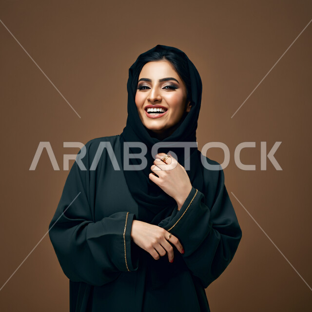 مفهوم النعومة والأنوثة، الشياكة والأناقة والاعتناء بالمظهر الخارجي، بورتريه مقرب لأمراة عربية خليجية سعودية محجبة مبتسمة ترتدي العباءة السوداء تنظر الى الكاميرا بتعابير الفرح والسعادة والسرور، خلفية بني