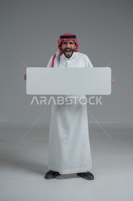 لوح إعلاني فارغ، موك اب أبيض، بورتريه لرجل عربي خليجي سعودي يرتدي الثوب التقليدي والشماغ يحمل بيده لوحه بيضاء، الوقوف باستقامه بايماءات الثقة بالنفس، صورة الجسم بالطول الكامل، خلفية رماديه