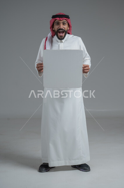 موك اب أبيض، لوح إعلاني فارغ،  بورتريه لرجل عربي خليجي سعودي يرتدي الثوب التقليدي والشماغ يحمل بيده لوحه بيضاء، الوقوف باستقامه بايماءات الثقة بالنفس، صورة الجسم بالطول الكامل، خلفية رماديه