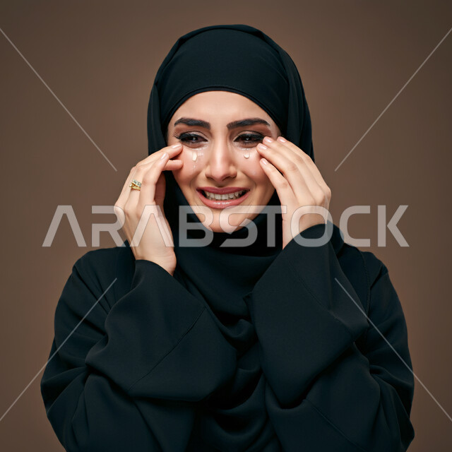 ايماءات الحزن واليأس، الشعور بالإنزعاج والخذلان والاكتئاب، بورتريه مقرب لإمرأة عربية خليجية سعودية ترتدي العباءة السوداء تضع يدها على وجهها بتعابير البكاء، فقدان وخسارة شيء ما، خلفية بنية