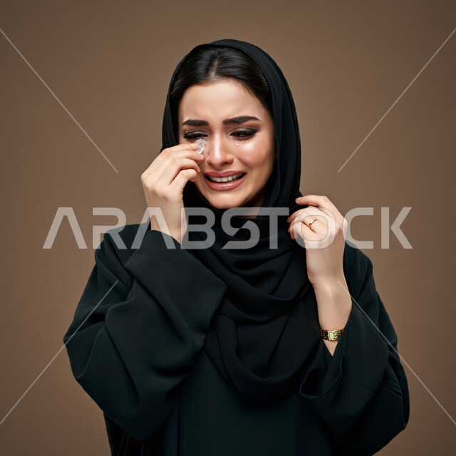 ايماءات الحزن واليأس، الشعور بالإنزعاج والخذلان والاكتئاب، بورتريه مقرب لإمرأة عربية خليجية سعودية ترتدي العباءة السوداء تضع يدها على وجهها بتعابير البكاء، فقدان وخسارة شيء ما، خلفية بنية
