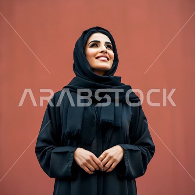  تعابير البهجة والسرور والسعادة، الاهتمام بالأناقة والمظهر الخارجي، مفهوم الأنوثة والنعومة، بورتريه مقرب لامرأة عربية خليجية سعودية محجبة مبتسمة ترتدي العباءة السوداء تنظر إلى الأعلى  بإيماءات الثقة بالنفس والفرح، خلفية حمراء
