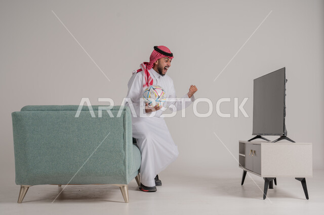 القفز فرحا وابتهاجا بإحراز هدف الفوز في الدوري، متابعة مباراة كرة القدم بتركيز وتمعن، بورتريه من الجانب لرجل عربي خليجي سعودي يستمتع بمشاهدة لعب فريقه المفضل، التفاعل مع الأهداف بسعادة وسرور، تنمية شغف الاهتمامات الرياضية، الجسم بالطول الكامل، خلفية رمادية