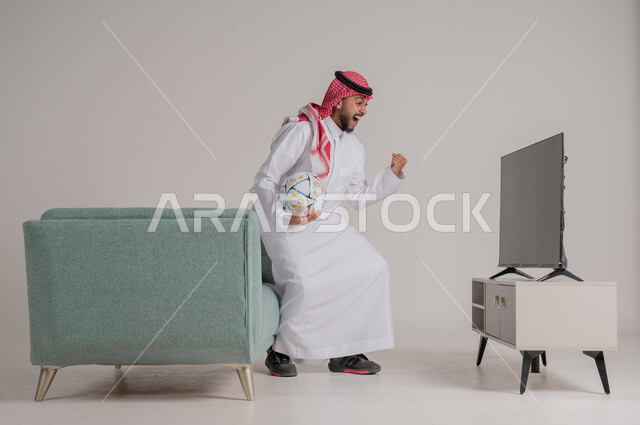 القفز فرحا وابتهاجا بإحراز هدف الفوز في الدوري، متابعة مباراة كرة القدم بتركيز وتمعن، بورتريه من الجانب لرجل عربي خليجي سعودي يستمتع بمشاهدة لعب فريقه المفضل، التفاعل مع الأهداف بسعادة وسرور، تنمية شغف الاهتمامات الرياضية، الجسم بالطول الكامل، خلفية رمادية