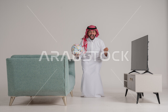 القفز فرحا وابتهاجا بإحراز هدف الفوز في الدوري، متابعة مباراة كرة القدم بتركيز وتمعن، بورتريه من الجانب لرجل عربي خليجي سعودي يستمتع بمشاهدة لعب فريقه المفضل، التفاعل مع الأهداف بسعادة وسرور، تنمية شغف الاهتمامات الرياضية، الجسم بالطول الكامل، خلفية رمادية