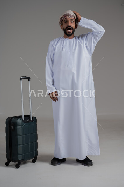 التأخر على موعد الانطلاق على موعد الانطلاق، مفهوم السياحة في إجازة الصيف، القيام بالجولات الترفيهية، بورتريه لشاب عربي عماني يرتدي الدشداشة والعمامة يضع يده على رأسه بتعابير الدهشة وبجانبه حقيبة الامتعة، الجسم بالطول الكامل, خلفية بيضاء