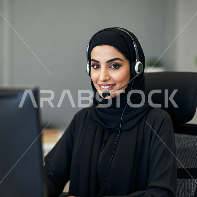 Working in the field of customer service in a company, a close-up photo of a smiling Saudi Arabian Gulf woman wearing an audio headset, inquiries and inquiries, answering customer questions, making a call through the laptop, holding a business meeting over the Internet.