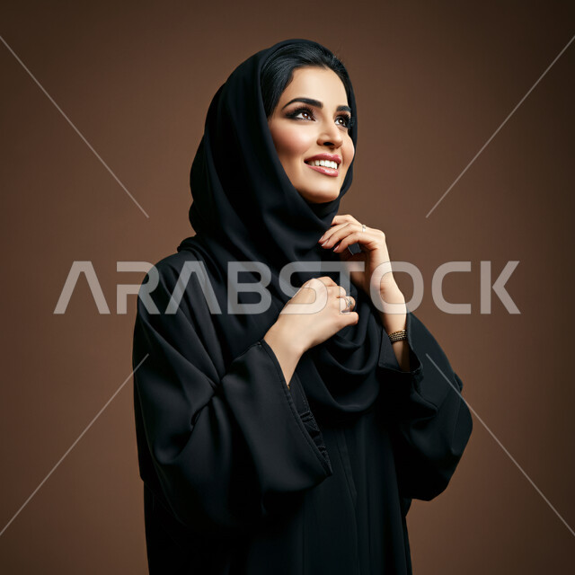 مفهوم الأنوثة والنعومة لدى النساء السعوديات، الشياكة والأناقة والاهتمام بالمظهر الخارجي, تعابير السعادة والسرور ، بورتريه مقرب لإمرأة عربية خليجية سعودية محجبة مبتسمة ترتدي العباءة السوداء تنظر إلى مكان ما في الأعلى بإيماءات الثقة بالنفس والفرح، خلفية بنية