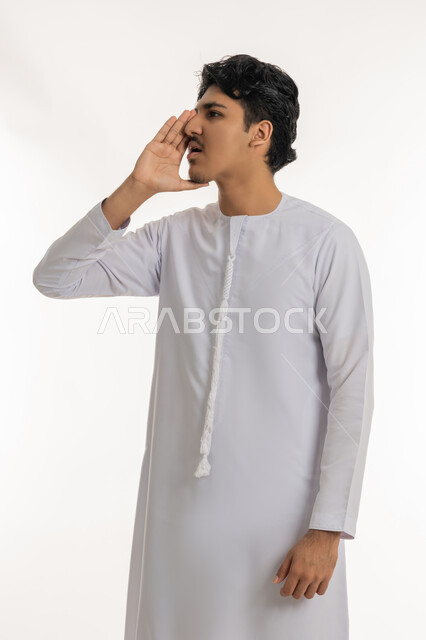 الهمس والهدوء اثناء الكلام، التحدث بصوت منخفض ، مفهوم المناداة بصوت مرتفع، بورتريه لشاب عربي خليجي إماراتي يرتدي الكندورة يقوم بالنداء خلف يده، كتمان وحفظ الاسرار، مشاركة سر ما، خلفية بيضاء