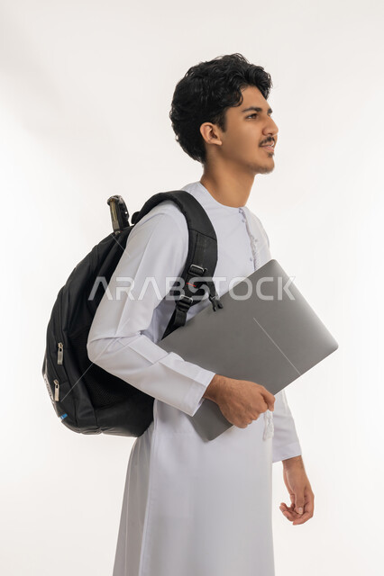 Developing educational curricula in the Emirates, following up on lessons and assignments, portrait of a young Emirati Gulf Arab man wearing a kandura carrying a backpack and school books, seriousness and diligence to achieve success and excellence, the importance of education in building the future, white background
