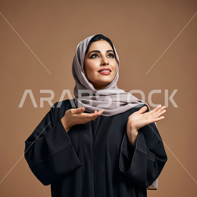 إشارات وحركات يدين تدل على هذا المكان (هنا)، محاولة تحديد موقع شيء معين، بورتريه لامرأة عربية خليجية سعودية ترتدي العباءة السوداء تشير بيديها إلى جهة اليسار، النظر والتأمل الى مكان ما في الاعلى بإيماءات الفرح والسرور، الأناقة والاهتمام بالمظهر الخارجي، خلفية بنية