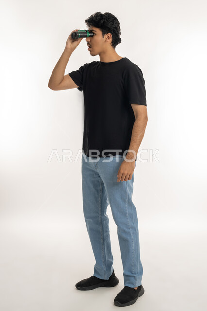 رؤية الاشياء البعيدة عبر المنظار، حب المغامرة والاستكشاف، التخطيط المستقبلي للأهداف والطموحات، بورتريه لشاب عربي خليجي إماراتي يرتدي الزي الكاجوال ينظر من خلال منظار الرؤية, الطول الكامل للجسم، خلفية بيضاء