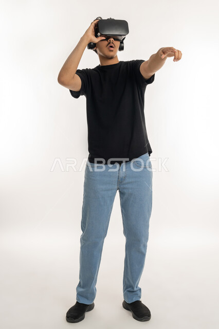 رؤية مستقبلية بعيدة، بورتريه لشاب عربي خليجي إماراتي يتدي الزي الكاجوال ونظارات الواقع الافترضي ثلاثية الابعاد يشير بإصبع السبابة الى مكان بعيد، أجهزة تكنولوجية وتقنيات حديثة، محاكاة العالم الخيالي، الطول الكامل للجسم، خلفية بيضاء