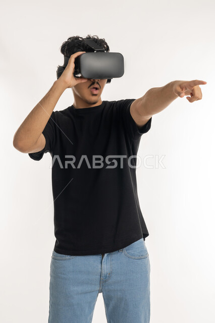 Modern technological devices and technologies, distant future vision, Portrait of a young Arab Gulf Emirati man Casual wear and 3D virtual reality glasses pointing index finger to distant place, simulated fantasy world, white background