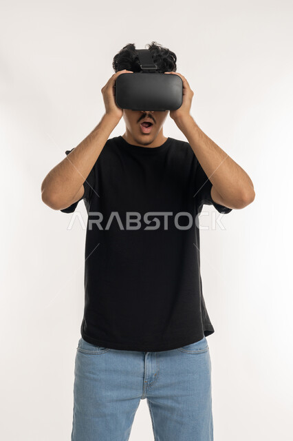 التسلية بالمشاهدة عبر نظارة الواقع الافتراضي، بورتريه لشاب عربي خليجي إماراتي يرتدي الزي الكاجوال ينظر من خلال نظارات ثلاثية الأبعاد (الفي ار), الاندماج ومحاكاة العالم الخيالي والنظر الى الافلام الواقعيه، التطور التقني والتكنولوجي, خلفيه بيضاء