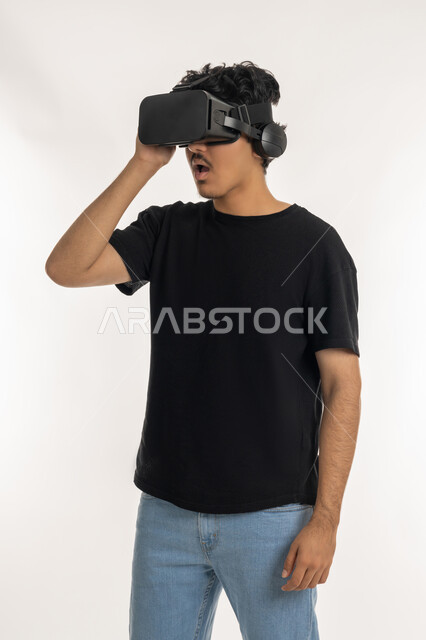 Integrating technology into practical life, merging and interacting with the virtual world, enjoying spending leisure time using modern electronic technologies, portrait of a young Arab Gulf Emirati man wearing casual clothes wearing 3D VR glasses, white background