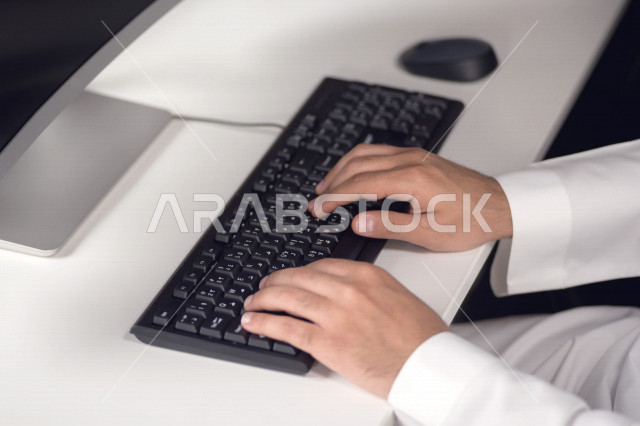 Close-up of the hand of a Saudi Arabian Gulf man working in customer service, inquiries and inquiries, answering customer questions, making video call through the computer, follow-up and development of work, data entry