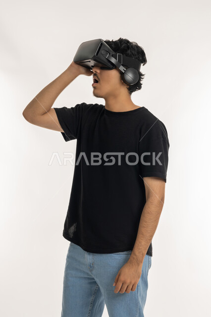 Technical and technological development, Enjoyment and entertainment by watching through virtual reality glasses, Portrait of a young Arab Gulf Emirati man wearing casual clothes looking through 3D glasses (VR), Integration and simulation of the imaginary world and watching real movies, white background