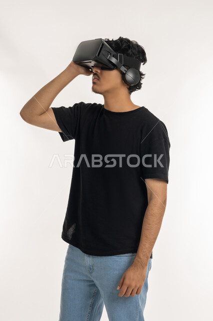 الاستمتاع في قضاء الأوقات الترفيهية عبر استخدام التقنيات الحديثة الالكترونية، بورتريه لشاب عربي خليجي إماراتي يرتدي الزي الكاجوال يضع نظارات الفي آر ثلاثية الابعاد، الاندماج والتفاعل مع العالم الافتراضي، دمج التكنولوجيا بالحياة العملية، خلفية بيضاء