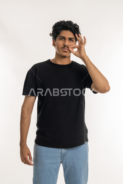 التهديد والتوعد لشيء ما، الاعجاب بنمو الشارب، بورتريه لشاب عربي خليجي إماراتي يرتدي الزي  الكاجوال ينظر الى الكاميرا ويمسك شاربه، إيماءات الالتزام والوفاء بالوعود، حركات وتعابير شبابيه، مفهوم الرجولة والقوة، خلفية بيضاء