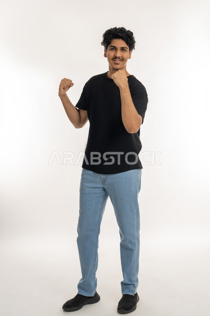 تعابير التفاعل والإندماج, بورتريه لشاب عربي خليجي إماراتي يرتدي الزي الكاجوال يرفع يديه مضموم الكفين, إيماءات السعادة والفوز والإنتصار, الشعور بالقوة والنجاح، أندية وتشجيع الفريق المفضل، الطول الكامل للجسم، خلفية بيضاء