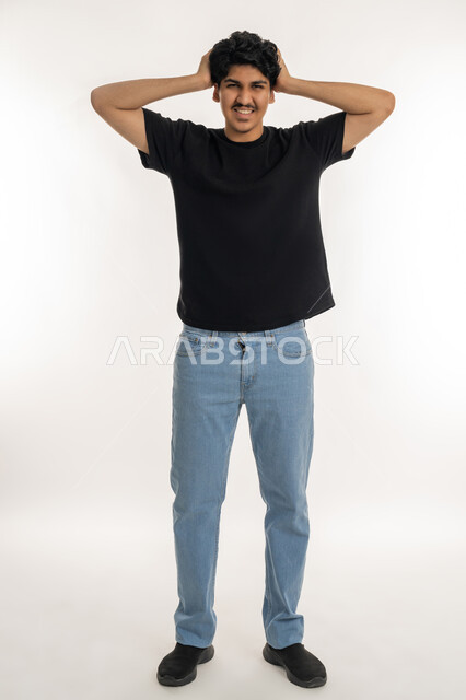 التفاجؤ والاستغراب من شيء ما، النظر إلى الكاميرا بإيماءات التعجب والدهشة، بورتريه لشاب عربي خليجي إماراتي يرتدي الزي الكاجوال يضع يديه خلف رأسه يشعر بالصدمة والذهول والانبهار، تعابير النجاح وتحقيق الأهداف, صورة الجسم بالطول الكامل، خلفية بيضاء