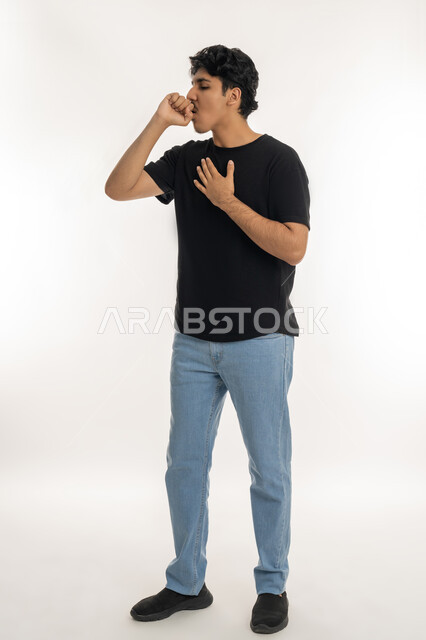 الإصابة بنزلة برد، الكحة والإنفلونزا والتهاب الحلق، بورتريه لشاب عربي خليجي إماراتي يرتدي الزي الكاجوال يضع يده على  صدره ويقوم بالسعال، الشعور بالم في الصدر، إيماءات المرض والتعب الحاجة للذهاب إلى الطبيب لتلقي العلاج المناسب، الطول الكامل للجسم، خلفية بيضاء