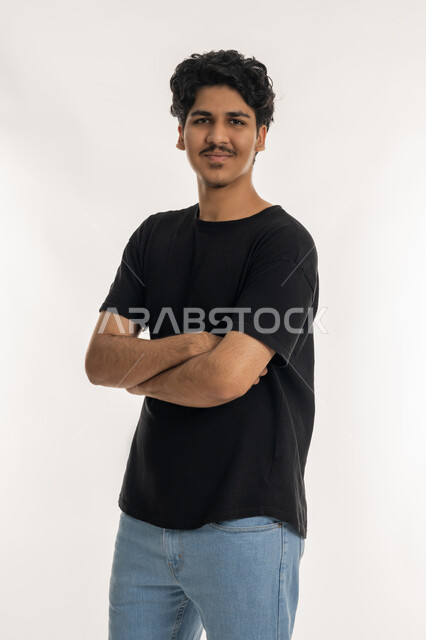 النظر إلى الكاميرا بإيماءات السعادة و السرور، تعابير الرجولة والثقة بالنفس, مفهوم الاناقة والشياكة،  الاهتمام بالمظهر الخارجي, بورتريه لشاب عربي خليجي إماراتي يرتدي الزي الكاجوال يقف بأيدي متقاطعة، خلفية بيضاء