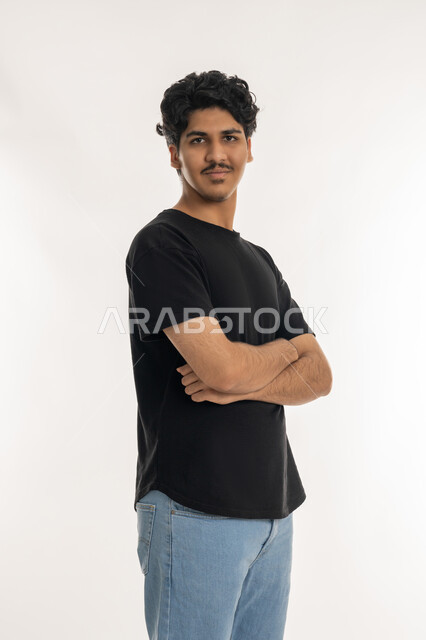 الاهتمام بالمظهر الخارجي, بورتريه من الجانب لشاب عربي خليجي إماراتي يرتدي الزي الكاجوال يقف بأيدي متقاطعة، النظر إلى الكاميرا بإيماءات السعادة و السرور، تعابير الرجولة والثقة بالنفس, مفهوم الاناقة والشياكة، خلفية بيضاء