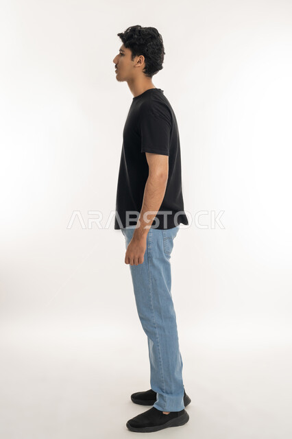 الوقوف باستقامة وثبات، مفهوم الرجولة العربية, النظر الى شيء ما بإيماءات الجدية،، بورتريه من الجانب لشاب عربي خليجي إماراتي يرتدي الزي الكاجوال ينظر إلى مكان محدد, الاهتمام بالأناقة والمظهر الخارجي، الطول الكامل للجسم، خلفية بيضاء