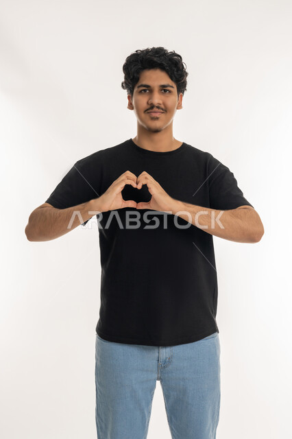 اظهار مشاعر الحب والشغف, مفهوم المحبة والمودة، ايماءات يدين على شكل قلب،, بورتريه لشاب عربي خليجي إماراتي مبتسم يرتدي الزي الكاجوال ينظر إلى الكاميرا بتعابير السعادة والفرح, خلفية بيضاء