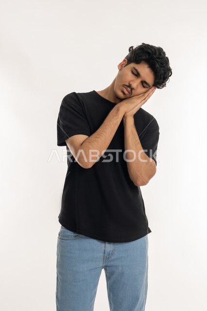 إغماض العينين والنوم بسلام، السهر لوقت متأخر من الليل، الشعور بالكسل والخمول و الارهاق، الحاجة للنوم والراحة، بورتريه لشاب عربي خليجي إماراتي يرتدي الزي الكاجوال يضع يديه تحت رأسه بإيماءات النعاس والتعب، خلفية بيضاء
