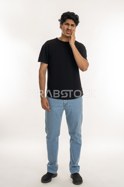 تسوس الأضراس وإلتهاب اللثه, الإحساس بوجع الأسنان والتألم من النخور، الحاجة للذهاب الى العيادة السنية لوضع الخطة العلاجية، الشعور بالتعب والمرض, بورتريه لشاب عربي خليجي إماراتي يرتدي الزي الكاجوال يضع يديه على خده بتعابير الألم, الجسم بالطول الكامل، خلفية بيضاء