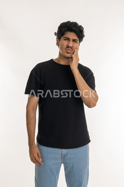 الحاجة للذهاب الى العيادة السنية لوضع الخطة العلاجية، الشعور بالتعب والمرض, بورتريه لشاب عربي خليجي إماراتي يرتدي الزي الكاجوال يضع يديه على خده بتعابير الألم, تسوس الأضراس وإلتهاب اللثه,  الإحساس بوجع الأسنان والتألم من النخور، خلفية بيضاء