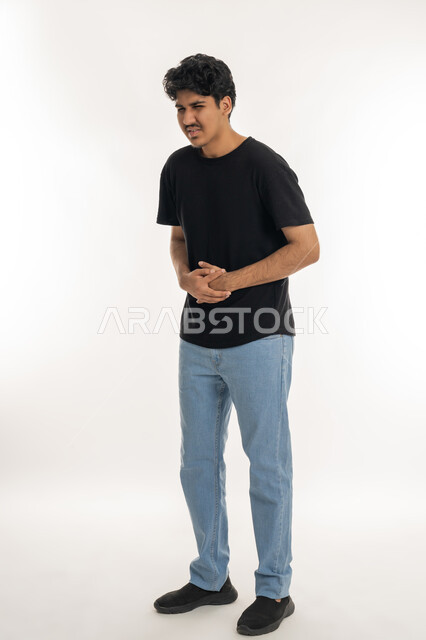 Feeling sick and having stomach ache, facial and hand movements indicating disturbance and discomfort, need for rest and appropriate treatment, portrait of a young Arab Gulf Emirati man wearing casual clothes, putting his hands on his stomach with an expression of pain, full body, white background
