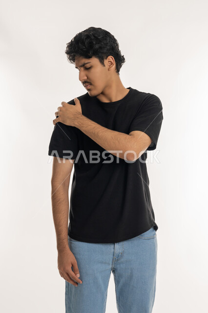 الأوجاع والآلام العصبية، طلب المساعده والحاجه للعلاج، بورتريه لشاب عربي خليجي إماراتي يرتدي الزي الكاجوال يضع يده على كتفه بايماءات الألم والتعب والأرهاق، حالة اسعافية طارئة، التهاب العضلات والمفاصل، خلفية بيضاء