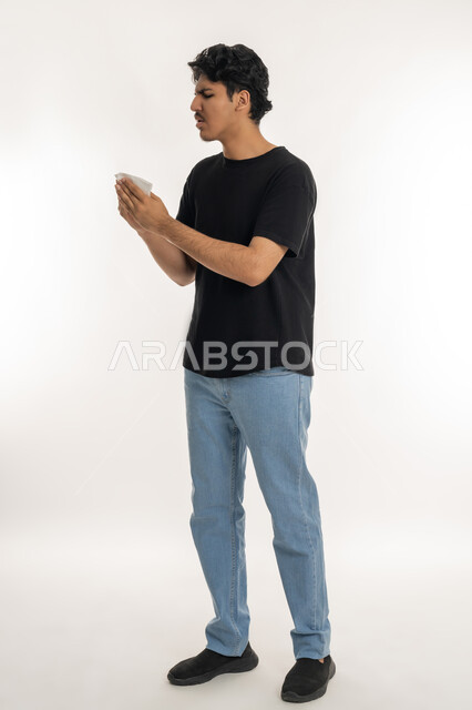 Feeling sick and cold, need for treatment and medicine, allergic rhinitis and sinusitis, portrait of a young Arab Gulf Emirati teenager in casual wear raising a tissue to his face with sneezing gestures, white background