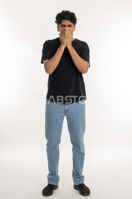 Allergic rhinitis and sinusitis, feeling sick and cold, need for treatment and medication, portrait of a young Arab Gulf Emirati teenager in casual wear putting his hands on his face with sneezing gestures, full body, white background